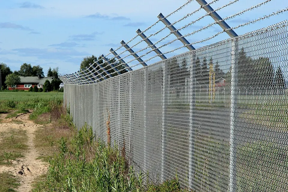 Tall galvanized chain link security fence with angled barbed wire arms